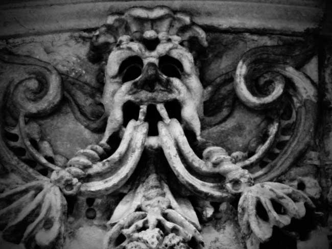 A scary looking stone face on an old City wall.